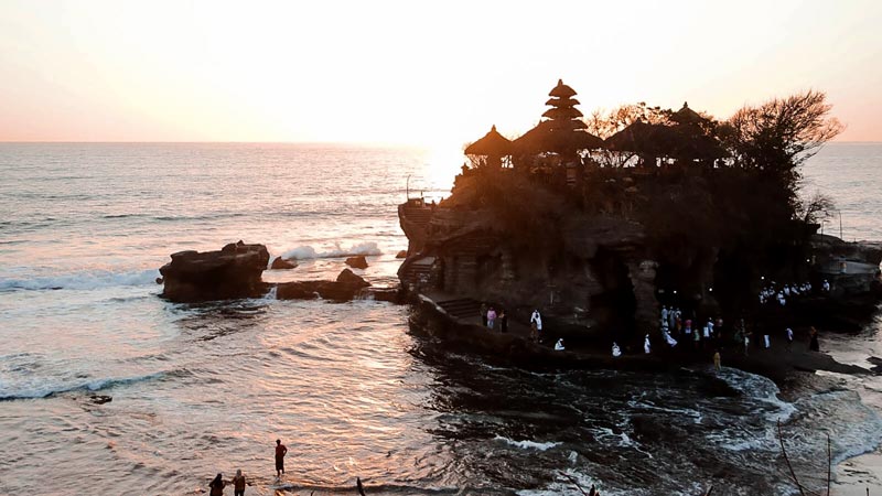 Pura Tanah Lot di Bali saat matahari terbenam, dengan ombak berdebur di sekelilingnya