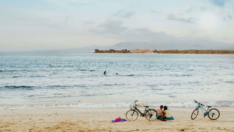 Pasangan sedang duduk di pantai kepulauan Gili Lombok sambil melihat laut dengan sepeda parkir di samping mereka