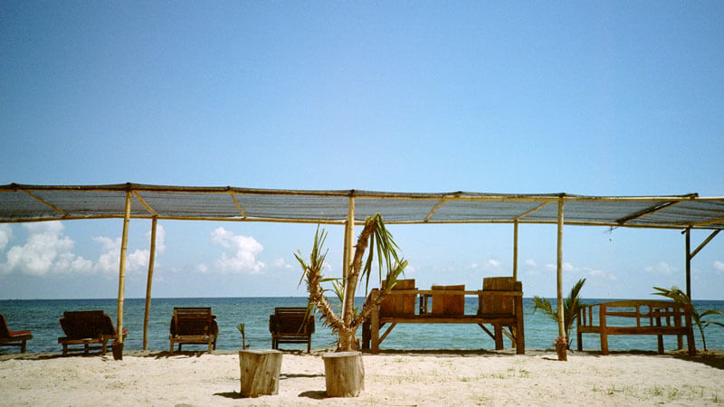 Tempat duduk kayu di bawah naungan tepi pantai Gili Air dengan latar belakang laut biru