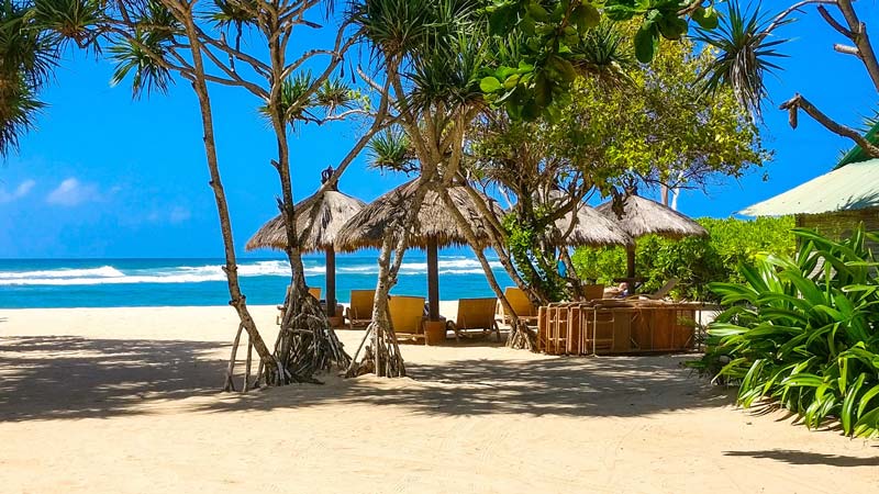 Pantai Nusa Dua dengan saung dan pohon palem yang menyediakan tempat teduh di tepi pantai berpasir putih