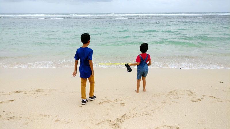 Dua anak kecil berdiri di tepi Pantai Melasti Ungasan, memandang ke lautan biru