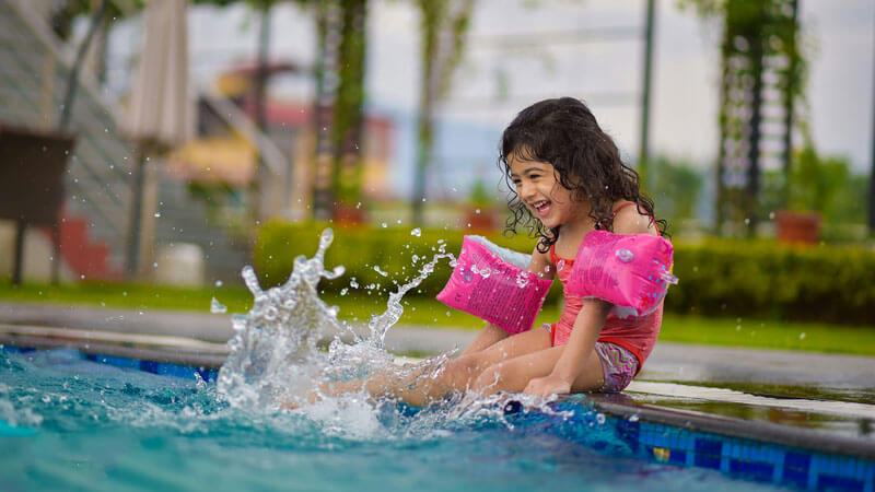 Anak perempuan ceria bermain air dengan pelampung di kolam renang. Tips Liburan Ke Bali Dengan Balita