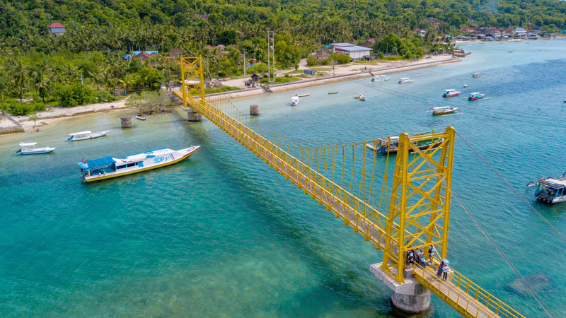 Jembatan Kuning ikonis di Nusa Lembongan, Bali, dengan latar belakang laut biru dan perahu