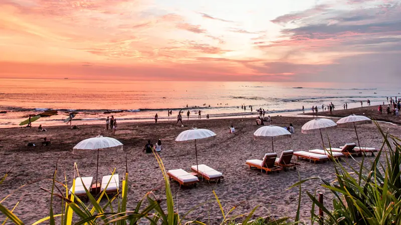 Pemandangan matahari terbenam dengan kursi pantai dan payung di Canggu