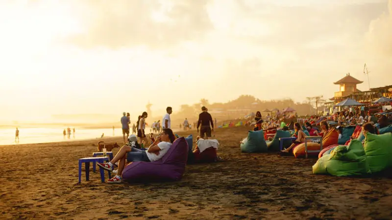 Pengunjung bersantai di atas bean bag saat matahari terbenam di Pantai Batu Bolong