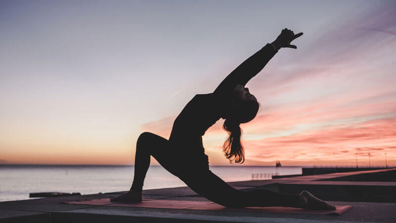 Wanita melakukan yoga peregangan di pantai dengan matahari terbit