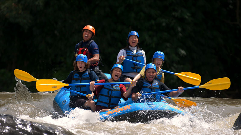 Kelompok wisatawan menikmati rafting di Sungai Ayung dengan perahu biru dan pemandu rafting