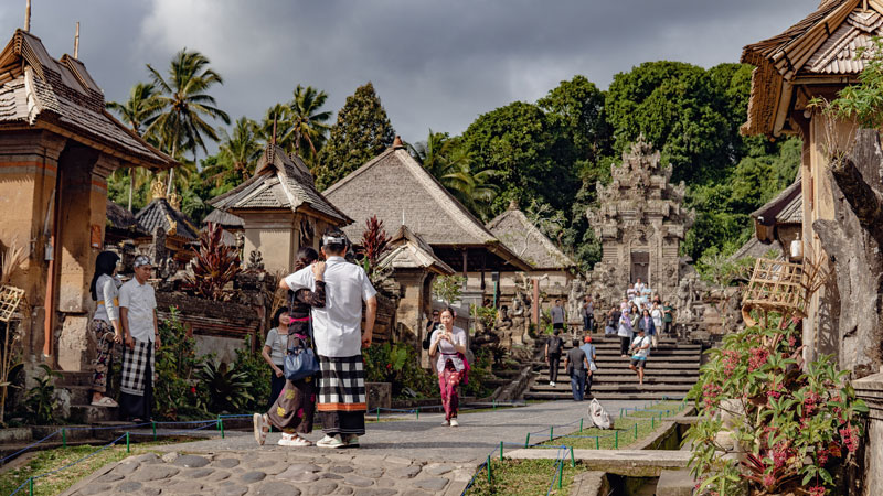 Pengunjung berjalan di jalan setapak Desa Penglipuran dengan latar belakang arsitektur Bali