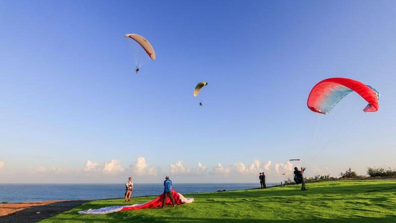 Paragliding di atas tebing Uluwatu, Bali, dengan pemandangan laut yang memukau.