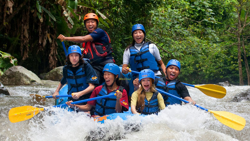 Wisatawan dalam aksi arung jeram di Bali, tertawa dan berdayung melalui jeram, mewakili petualangan yang sehat.