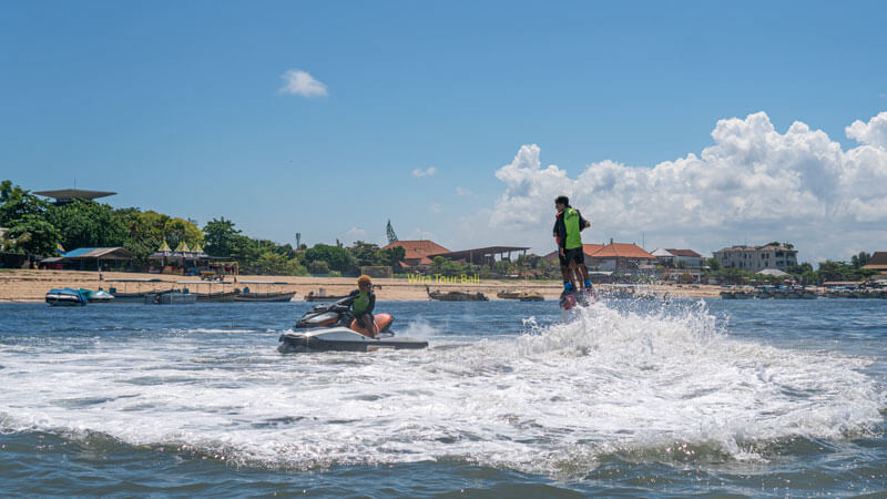 Pengalaman Flyboarding Seru di Bali, wisatawan menikmati aksi akrobatik di atas air dengan latar belakang pantai dan langit biru.