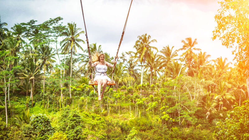 Seseorang berayun tinggi di atas hutan tropis di Ubud Swings. Aktivitas Liburan Seru di Bali