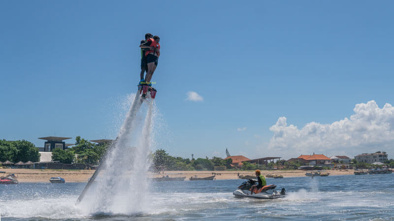 Wisatawan menikmati aktivitas flyboard di Pantai Tanjung Benoa dengan semburan air yang kuat mendorong mereka ke udara.