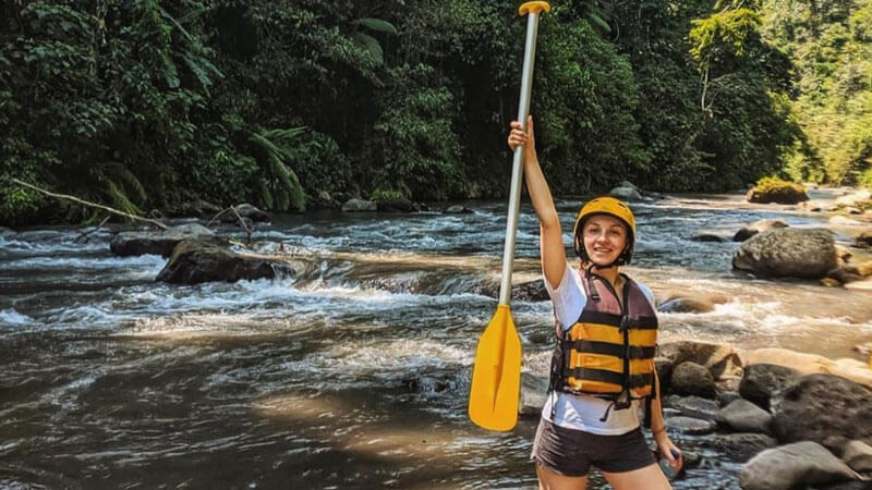 Wanita dengan pelindung kepala dan dayung siap untuk petualangan rafting di sungai Bali.