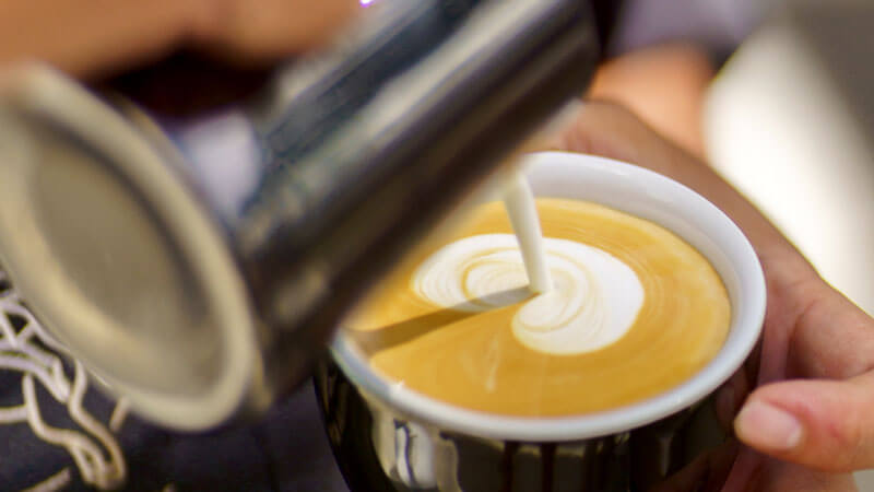 Menuangkan susu ke dalam kopi latte dengan latte art yang indah di Mitos Kopi Renon.