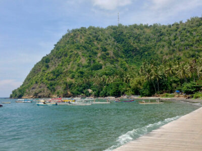 Pemandangan Pantai Labuhan Amuk dengan perahu-perahu dan latar bukit yang hijau