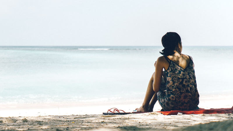 Wanita menikmati ketenangan saat duduk di tepi pantai