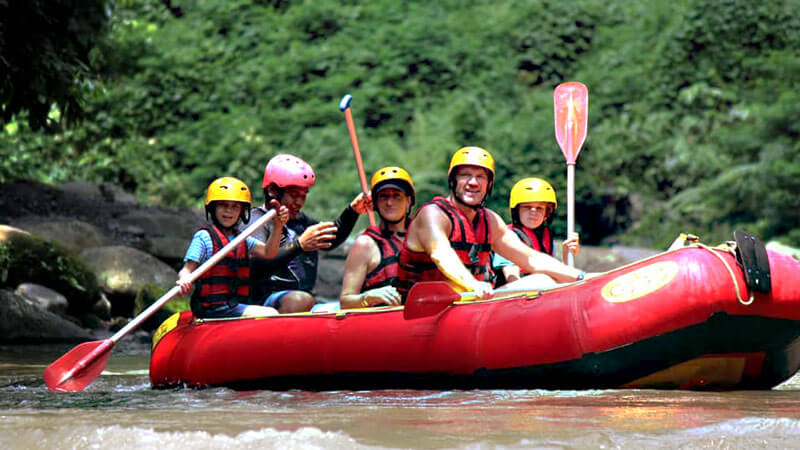 Keluarga dengan anak-anak kecil mengarungi arus Sungai Ayung, Ubud, dalam aktivitas rafting yang ramah keluarga.