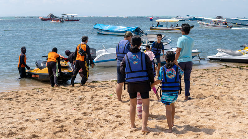 Wisatawan mengenakan jaket pelampung di tepi pantai sebelum berparasailing di Bali