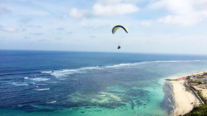 Keseruan paragliding di Bali dengan pemandangan laut.