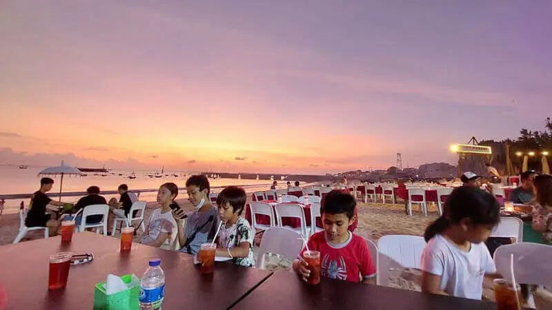 Wisatawan menikmati makan malam seafood di Pantai Jimbaran Bali saat sunset.