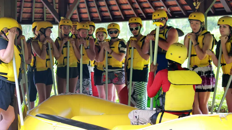 Pemandu memberikan instruksi kepada peserta rafting yang mengenakan helm dan jaket pelampung standar internasional.