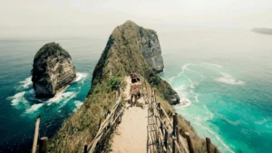 Wisatawan berjalan di jalur menurun menuju tebing T-Rex Pantai Kelingking dengan pemandangan laut biru di Nusa Penida.