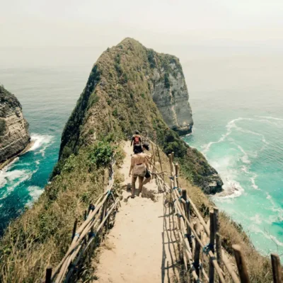 Wisatawan berjalan di jalur menurun menuju tebing T-Rex Pantai Kelingking dengan pemandangan laut biru di Nusa Penida.