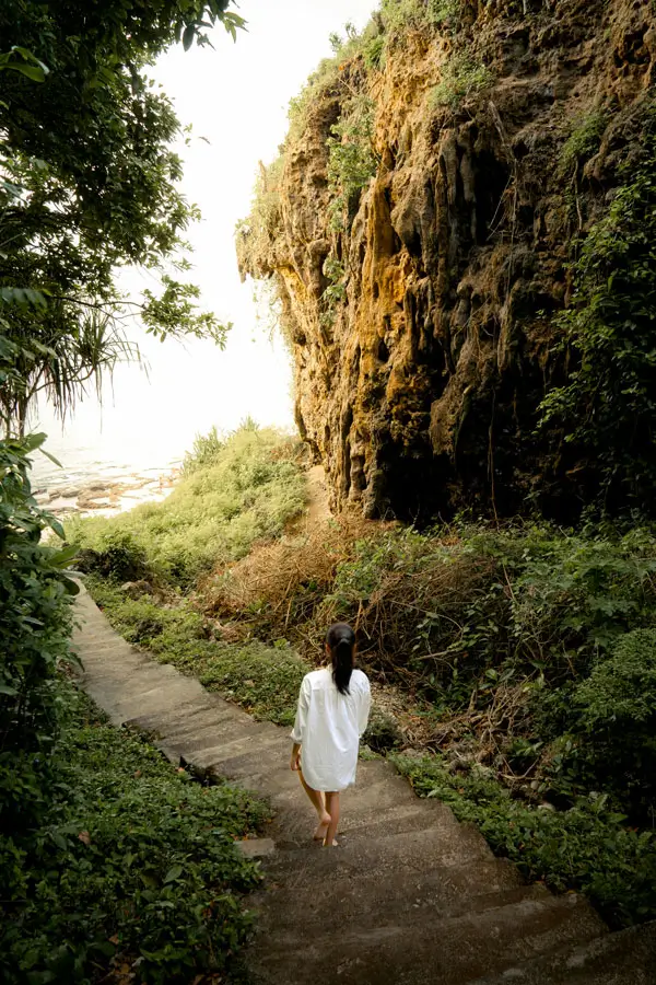 Tangga curam menuju pantai dari balik tebing hijau.