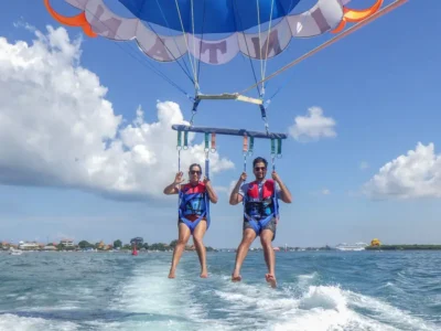 Pasangan pemula tersenyum dan melambaikan tangan saat parasailing di Tanjung Benoa Bali.