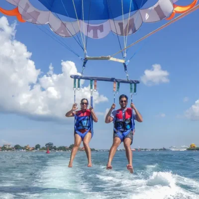 Pasangan pemula tersenyum dan melambaikan tangan saat parasailing di Tanjung Benoa Bali.