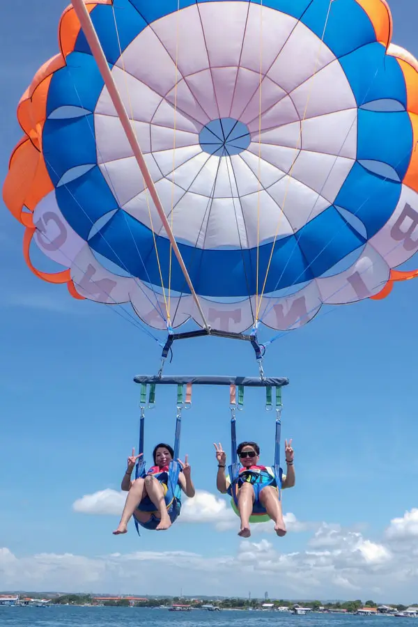 Dua wanita tersenyum sambil pose peace saat parasailing di Bali.