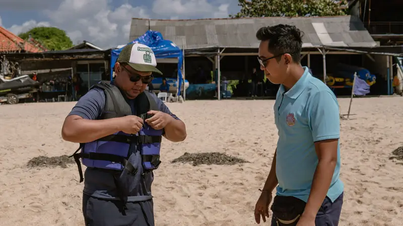Tim pemandu membantu tamu mempersiapkan perlengkapan keselamatan di area pantai.
