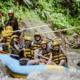Peserta rafting mengangkat dayung dengan ekspresi senang saat menyusuri Sungai Ayung