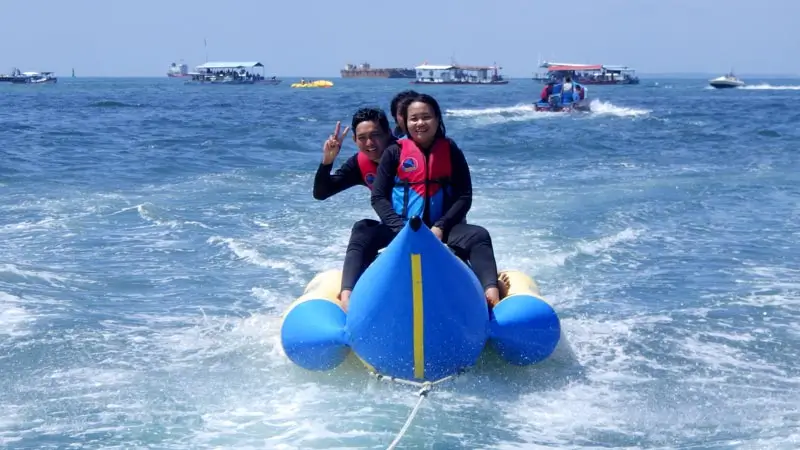 Pasangan di banana boat Bali dengan life jacket, ditarik speedboat