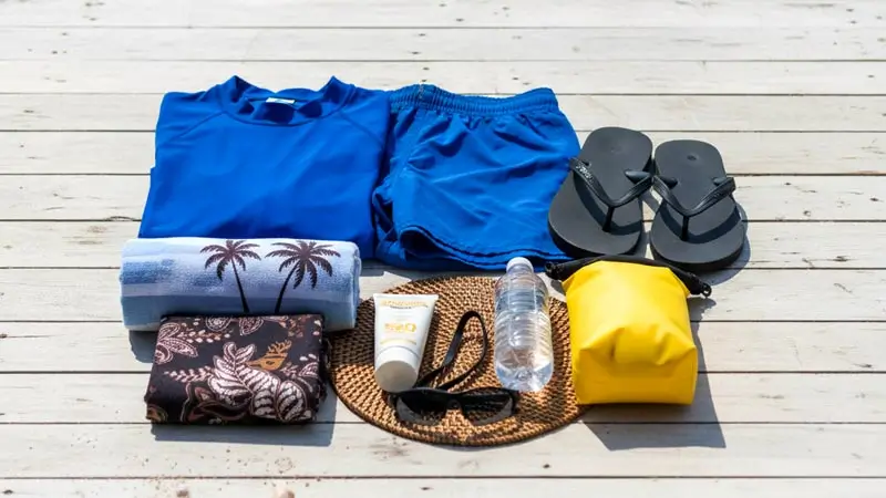 Perlengkapan banana boat: rash guard, celana renang, sandal, handuk, sunblock, botol air, dry bag