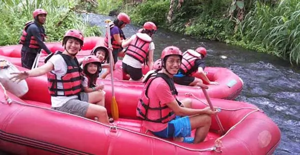 Keluarga Indonesia dan anak anak duduk di perahu rafting di sungai tenang Bali