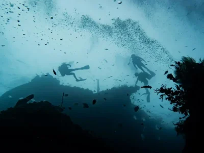 Siluet penyelam di atas bangkai kapal, gelembung naik di air biru