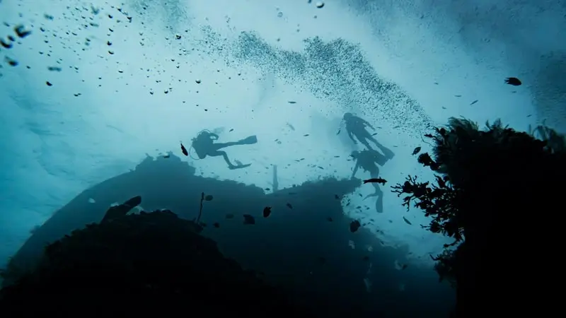 Siluet beberapa penyelam di atas bangkai kapal, gelembung naik ke permukaan