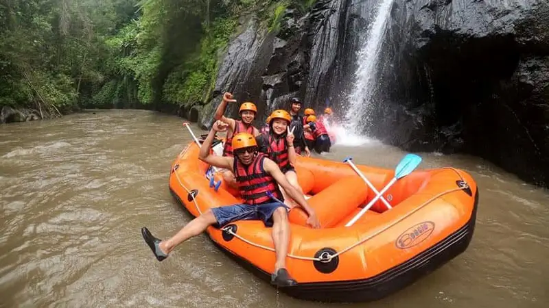Peserta arung jeram di perahu oranye melintas dekat air terjun di sungai